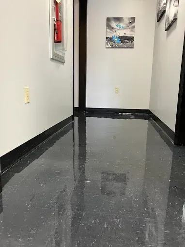 Narrow hallway with glossy black floor. White walls, fire extinguisher, and a photo on the wall.