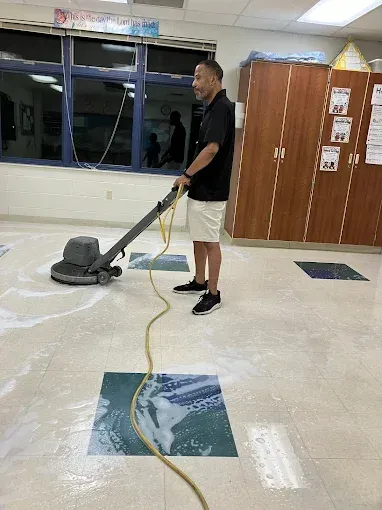 A person cleaning a classroom floor with a floor buffer.