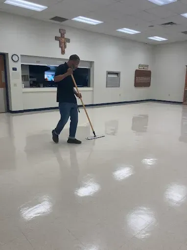 Man mopping a shiny, light-colored floor in a large room, likely a church hall.
