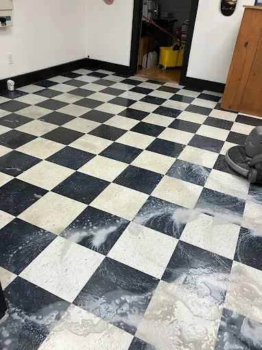 Black and white checkered floor being cleaned with a machine. Soap and water are visible on the floor.