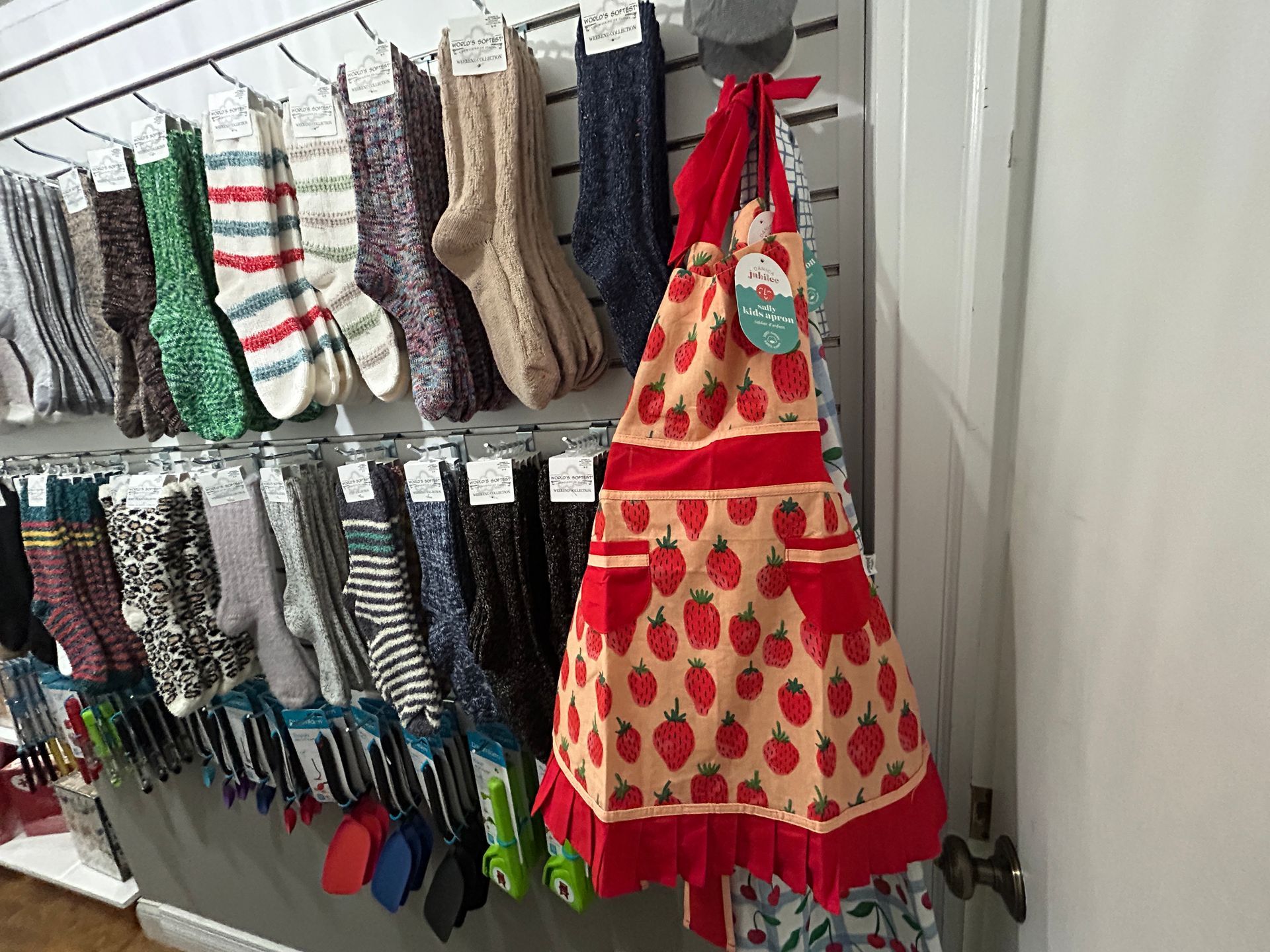 Socks and aprons hanging on a retail display rack, including a red strawberry-patterned apron