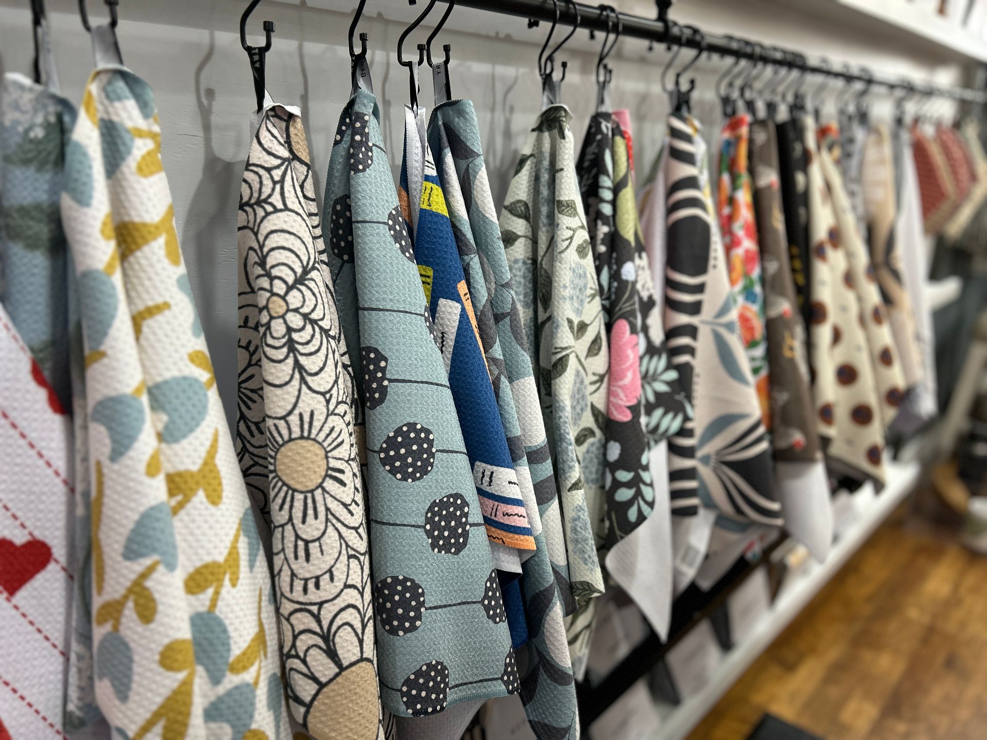 Assorted patterned towels hanging on a rack in a shop, with a wooden floor beneath