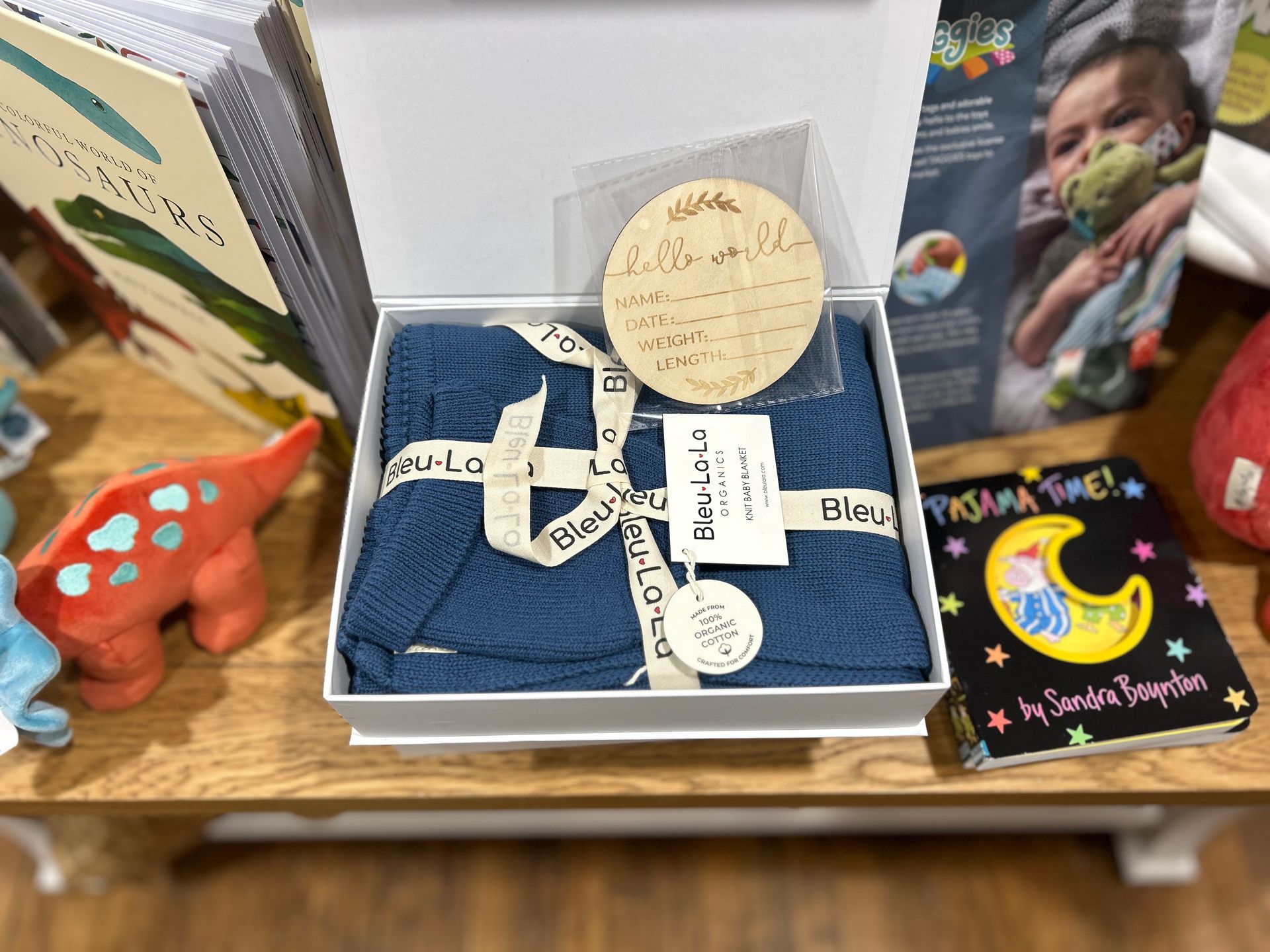Blue baby outfit gift box with white cross and round note, displayed on a table beside colorful cards