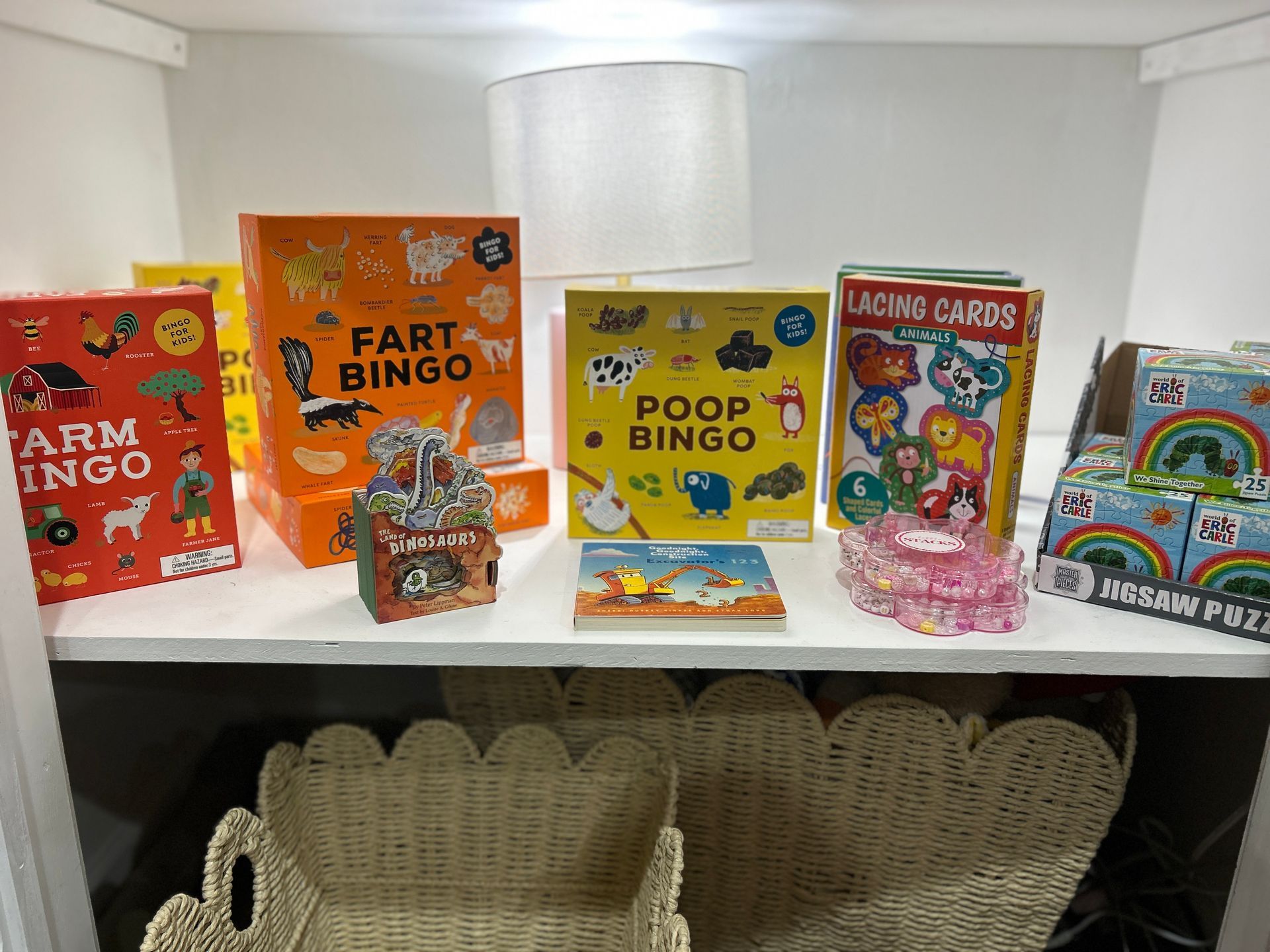 Colorful joke board games on a shelf, including Fart Bingo, Poop Bingo, and a fidget spinner display