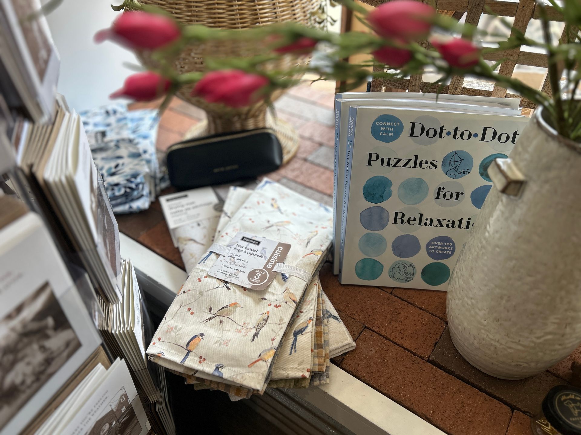 Books and puzzles on a table beside a vase of flowers and a woven basket