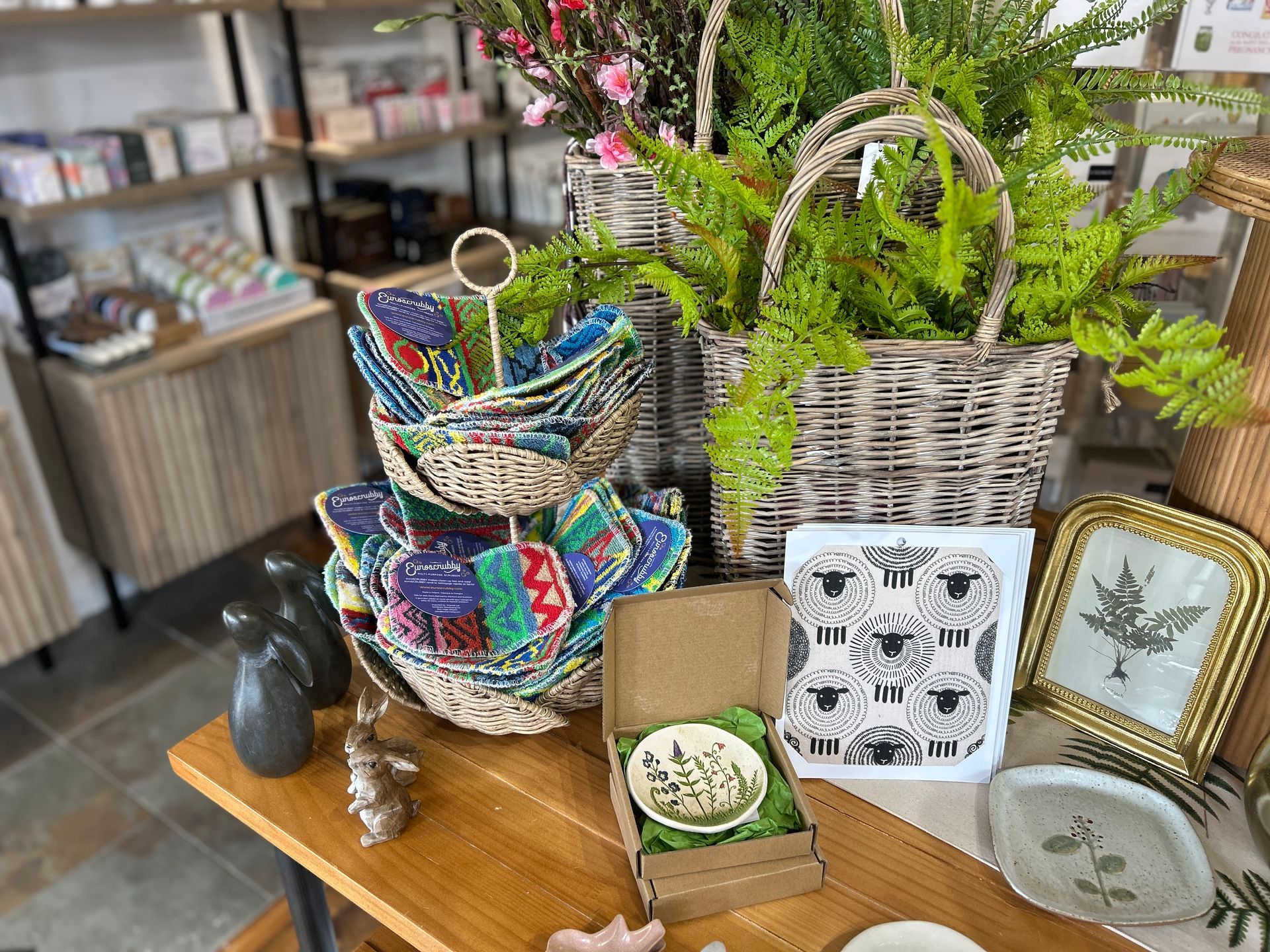 Assorted colorful woven baskets and framed decor displayed on a wooden table in a shop