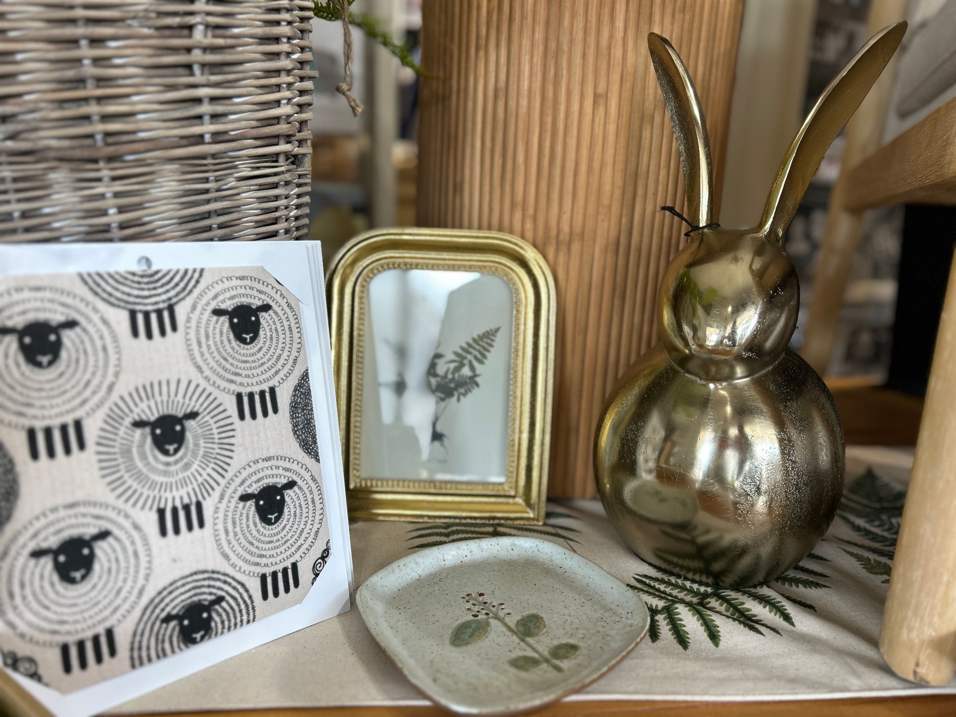 Decorative shelf vignette with woven basket, framed leaf print, gold bunny vase, and ceramic dish