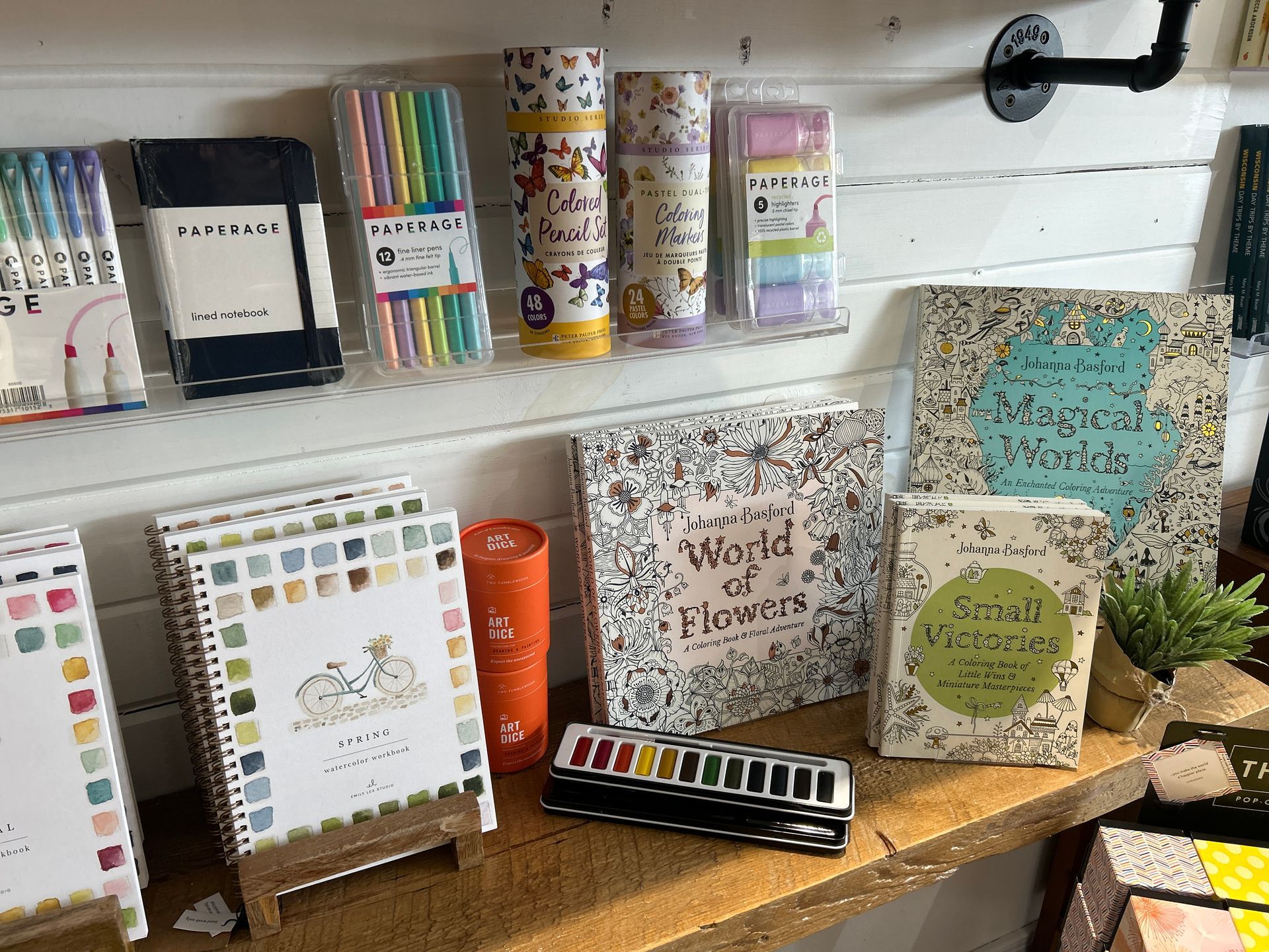 Desk display of colorful notebooks, planners, and framed crafts on a shelf in a cozy workspace.