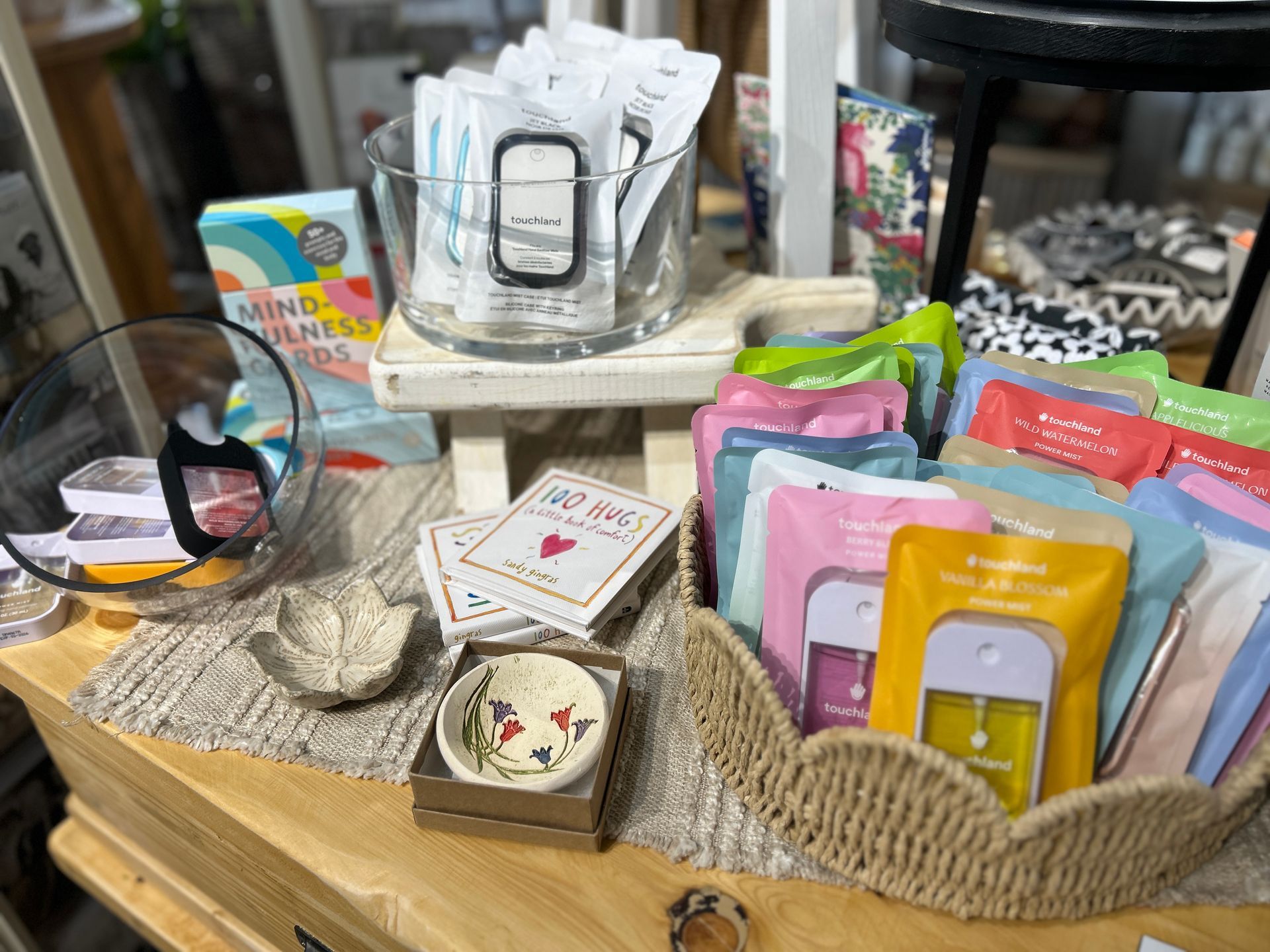Tabletop display of colorful packaged goods, glassware, and small decorative boxes on a wooden tray
