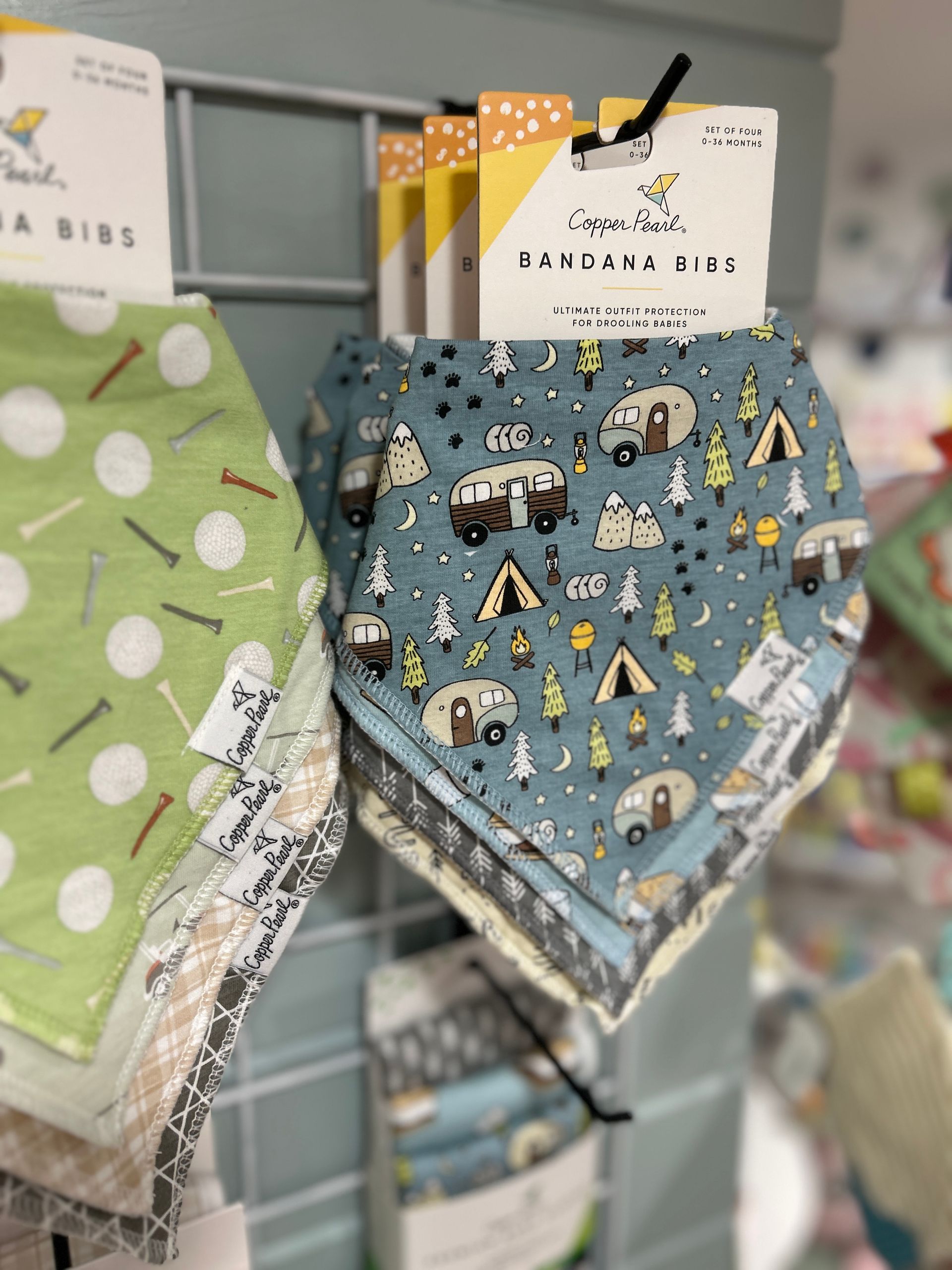 Patterned baby bibs hanging on a store rack, including blue, green, and plaid designs