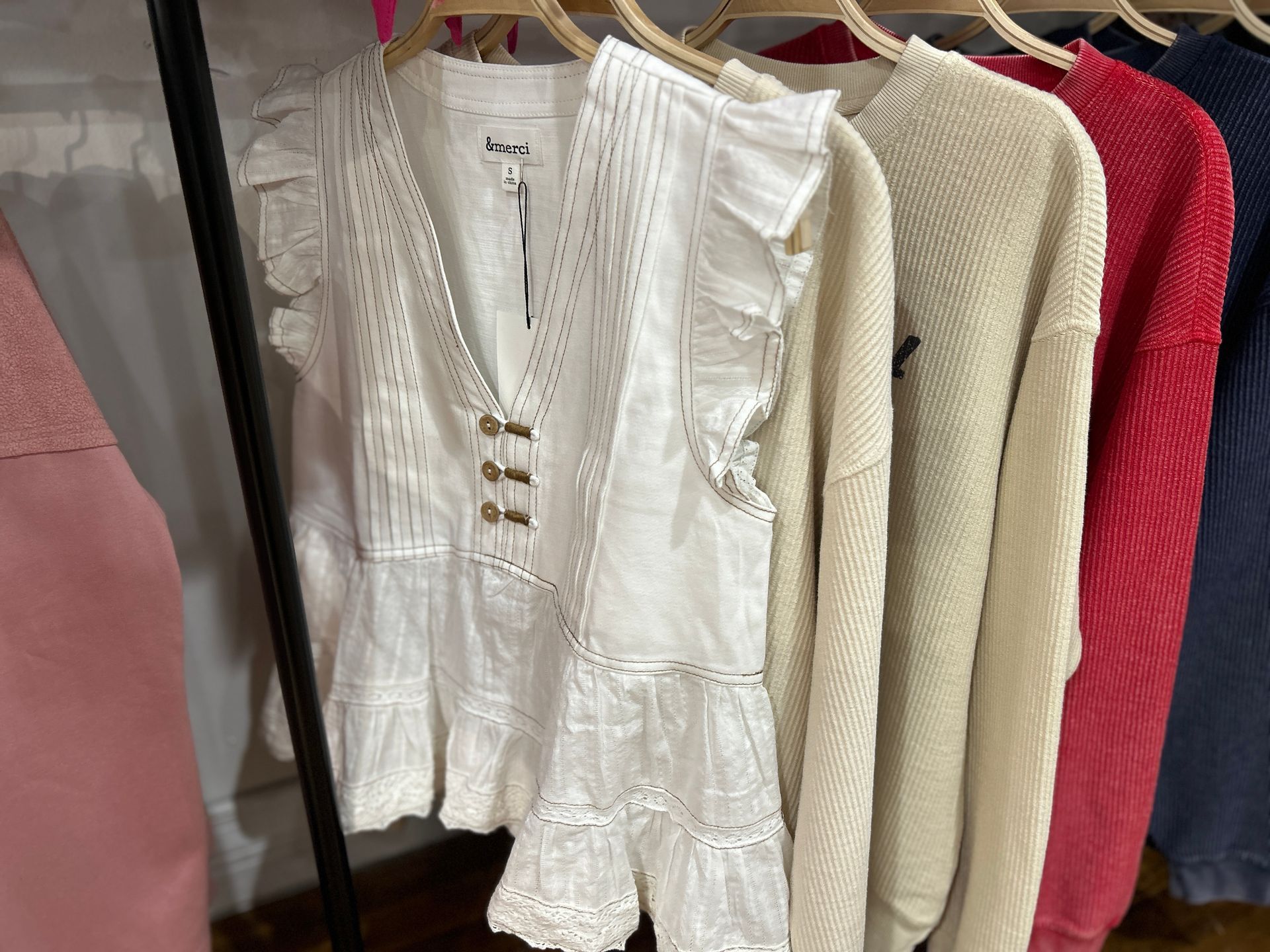 White ruffled blouse on a clothing rack beside cream and red sweaters