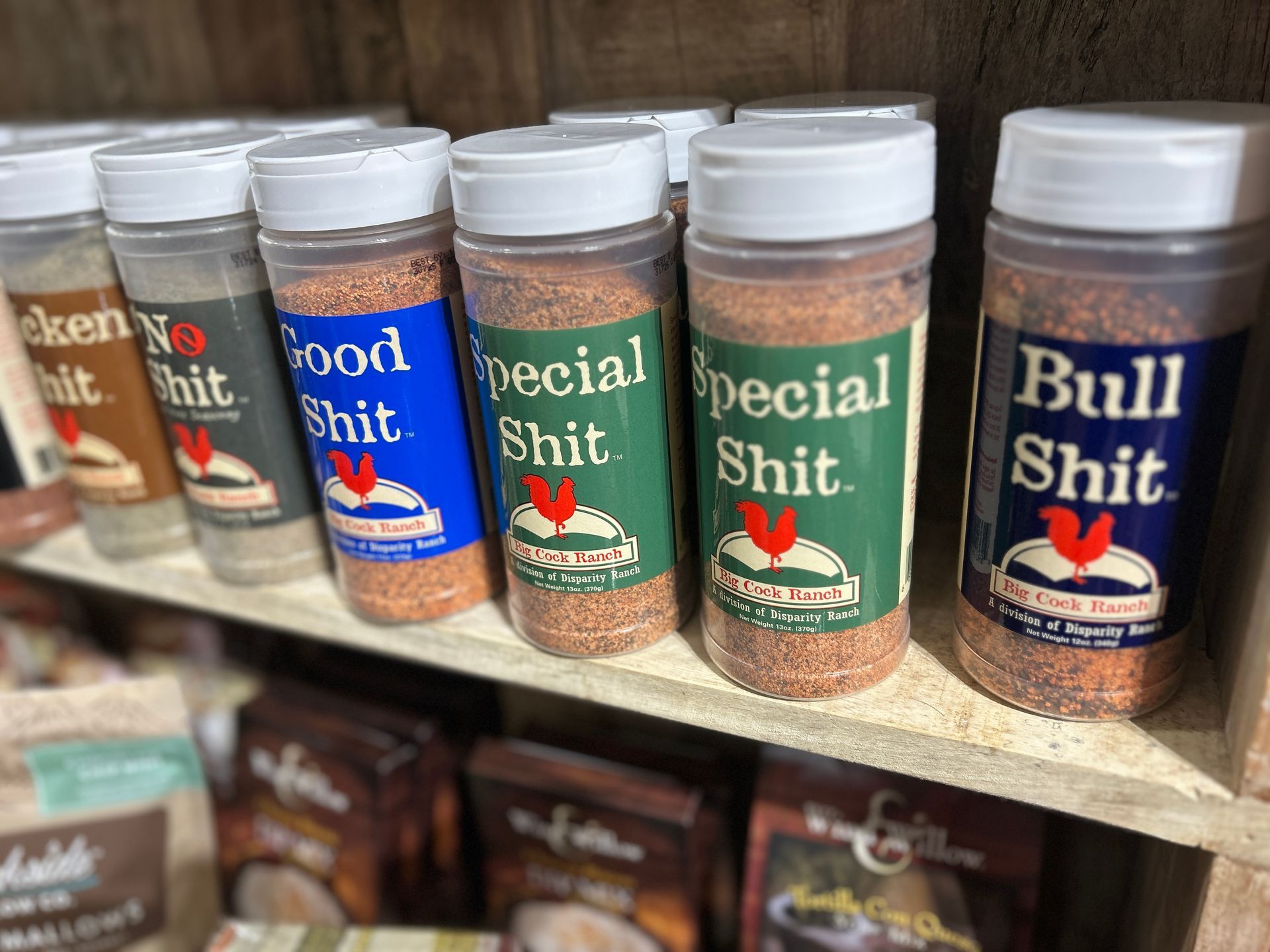Row of spice jars with humorous labels on a store shelf, including “Bull Shit” and “Good Shit”