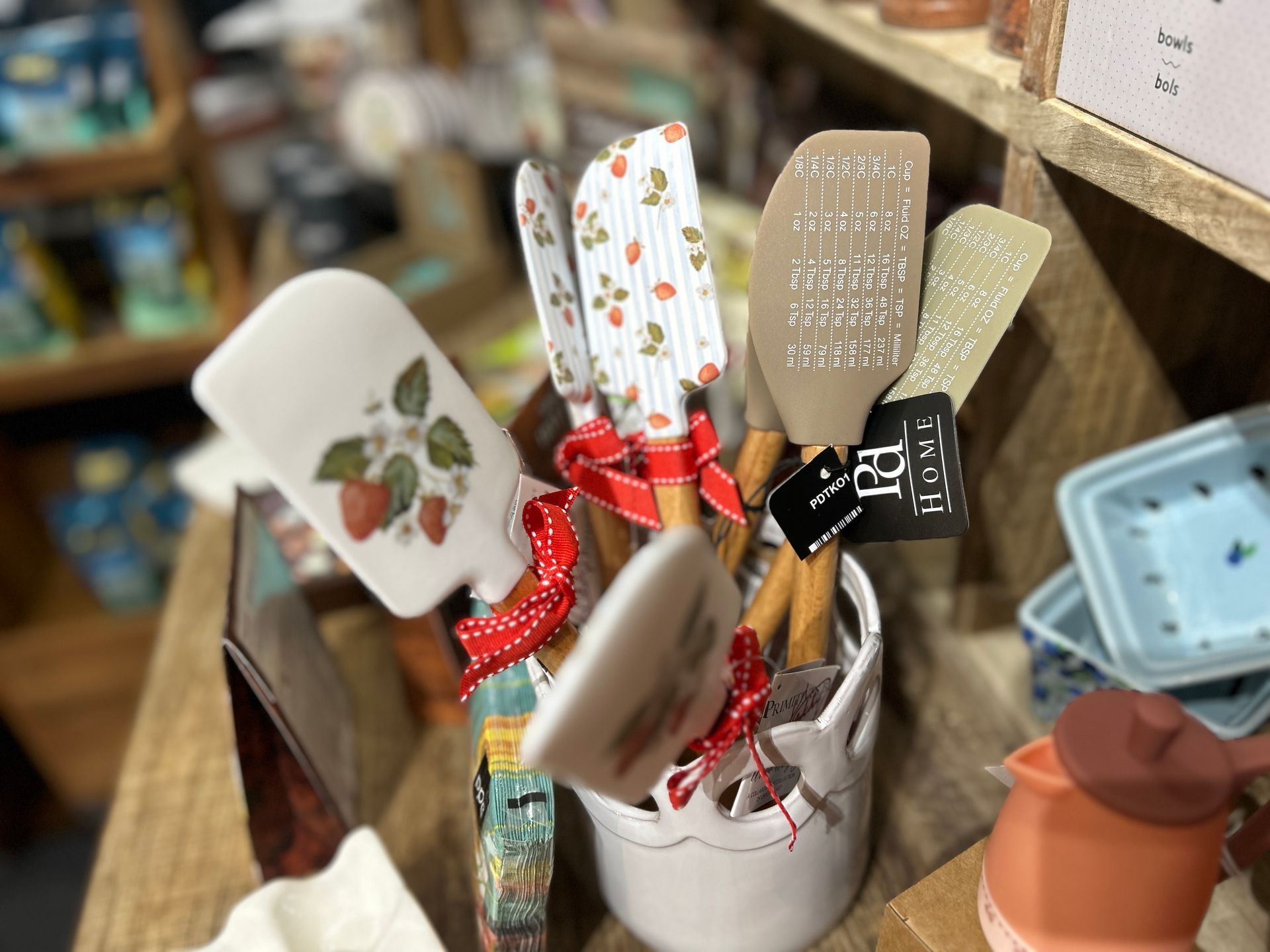 Assorted floral kitchen utensils in a white container on a shelf, with a small terracotta pot beside them