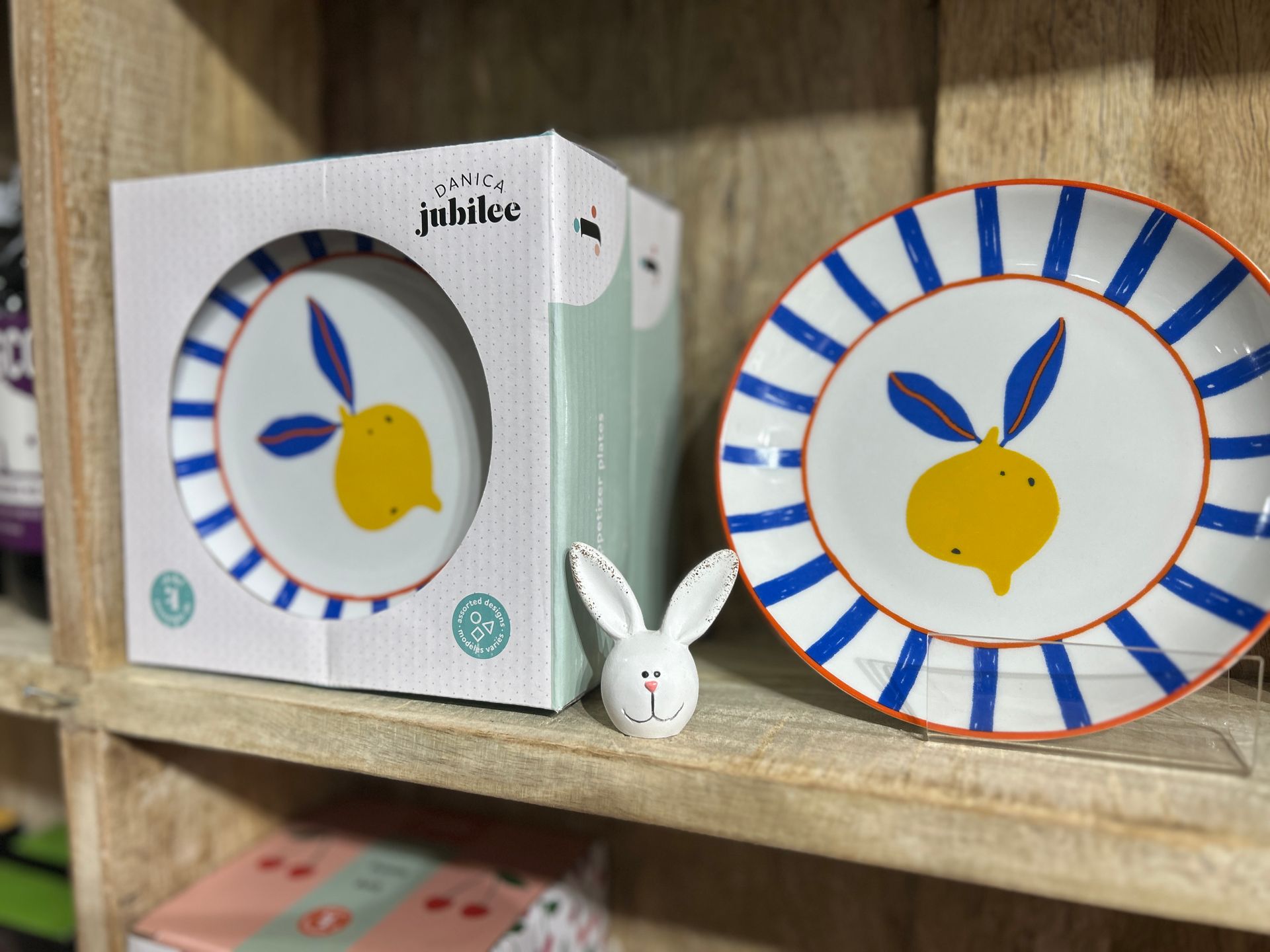 Rabbit-themed plate and box on a wooden shelf, with a small white bunny figurine in front