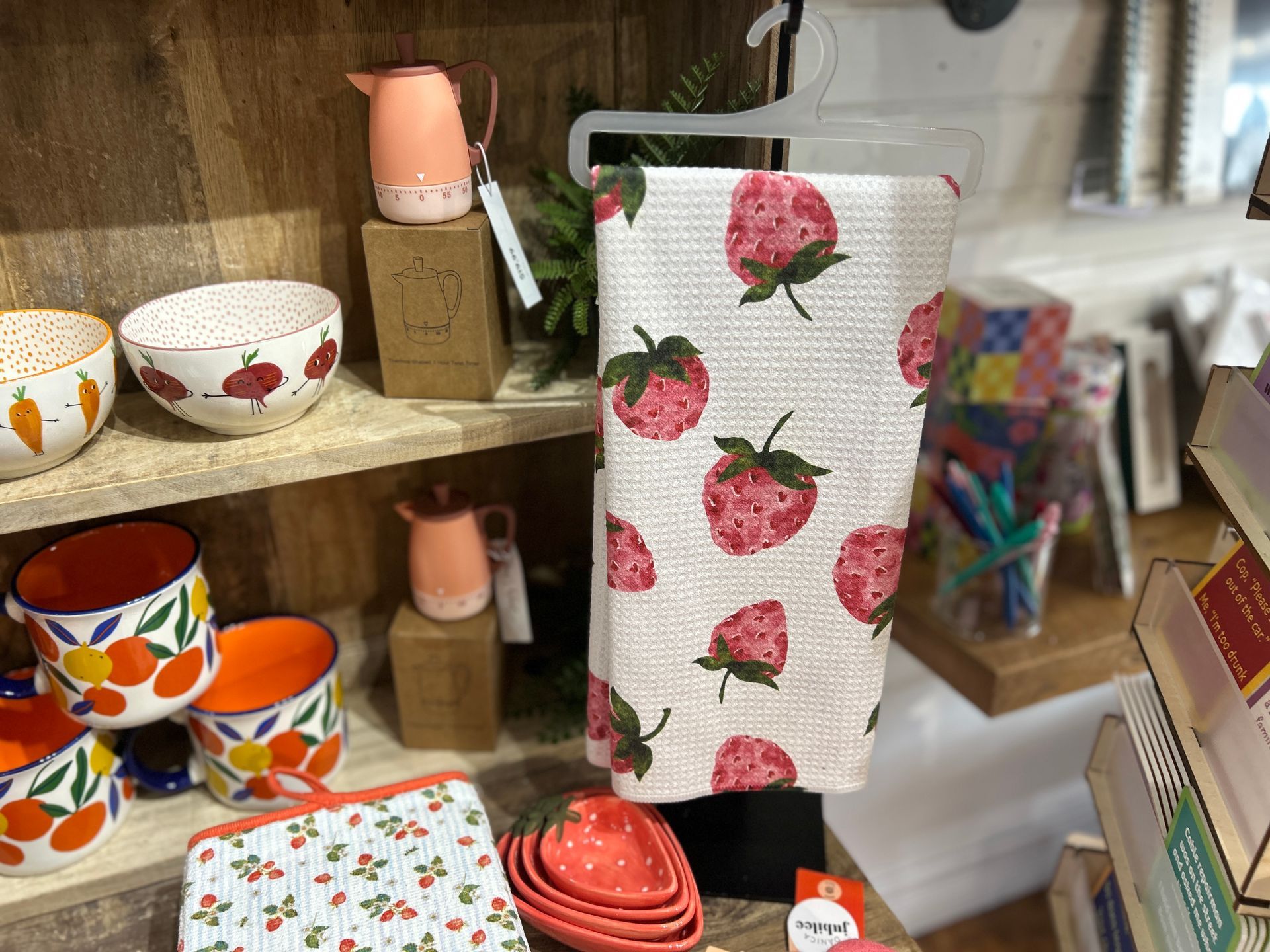 Shelved display of colorful ceramic bowls, cups, and strawberry-print textiles in a shop