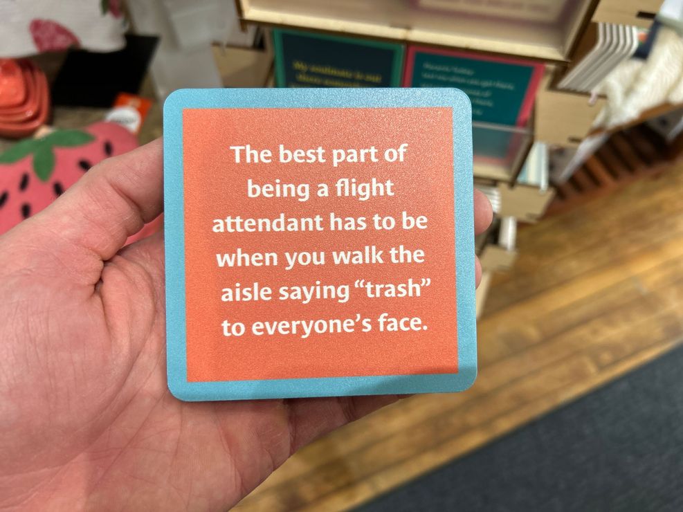 Hand holding a turquoise-and-coral sign that reads, “The best part of being a flight attendant…”