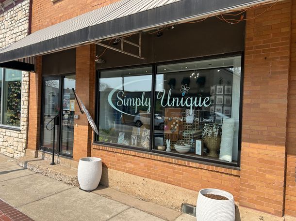 Storefront window with “Simple Unique” lettering, brick facade, and a sidewalk planter in front.