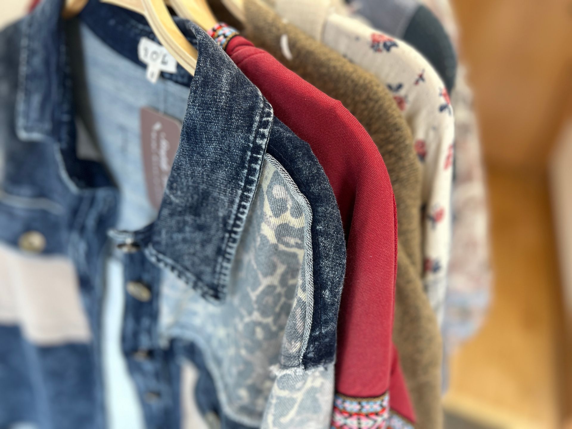 Clothes hanging on a rack, including denim and a red sweater, in a closet