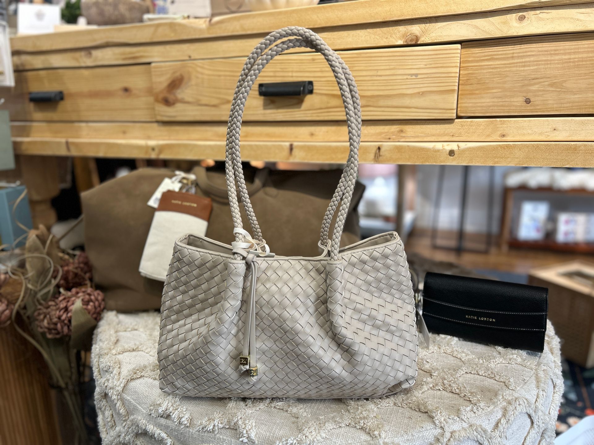 Gray woven handbag on a tabletop with wood drawers and a black wallet beside it