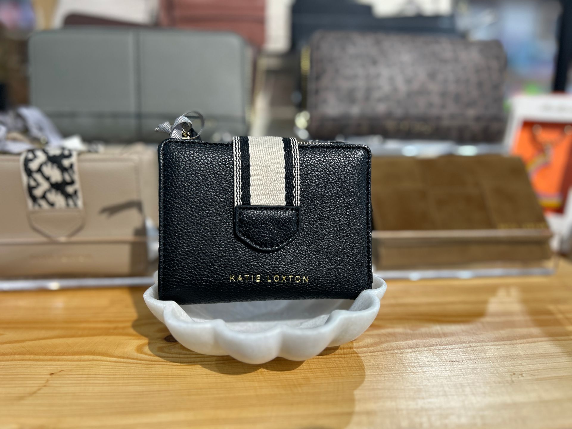 Small black glittery wallet with a white stripe, displayed on a white cushion on a wooden table.