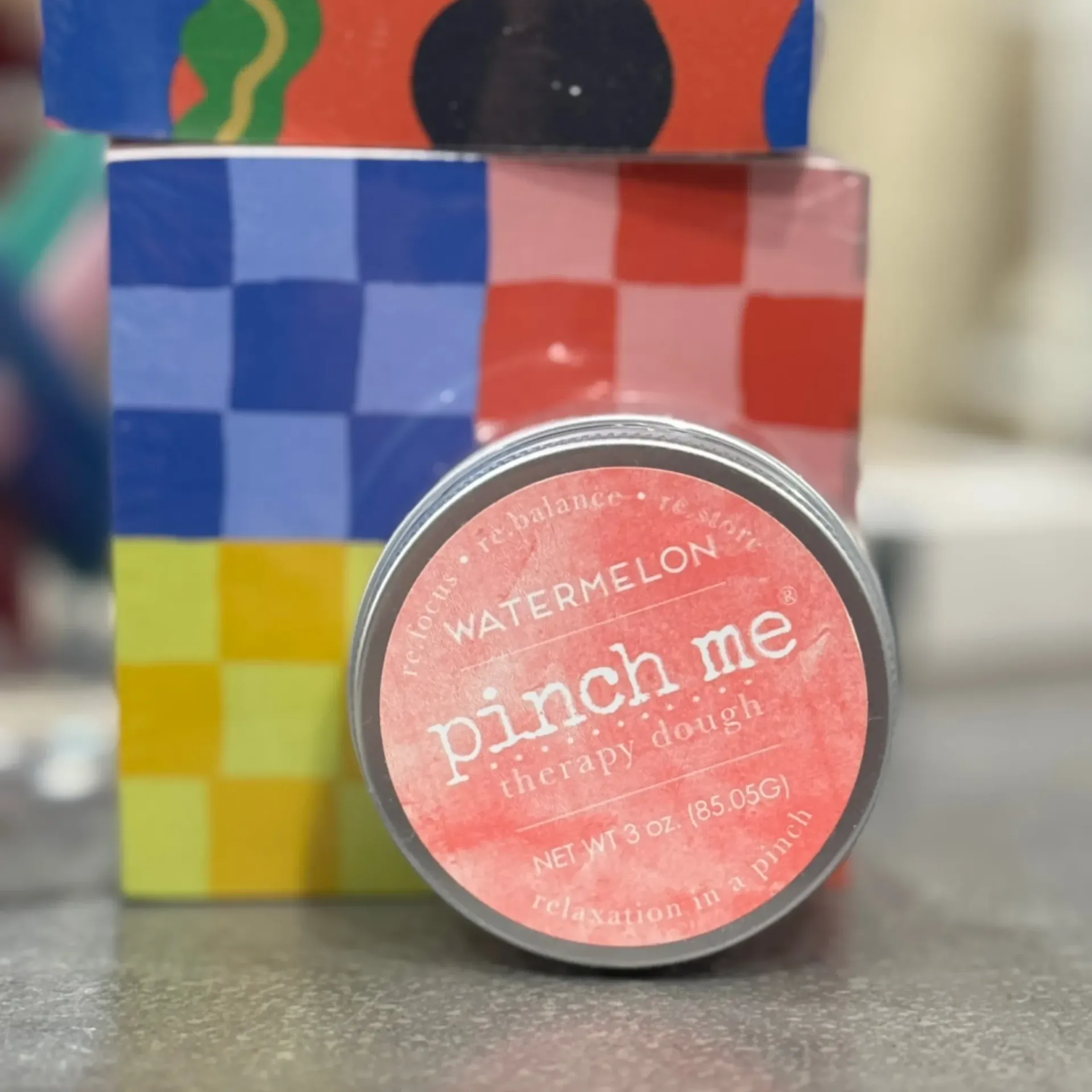 Pink “Watermelon” pinchme tin in front of colorful checkered gift boxes