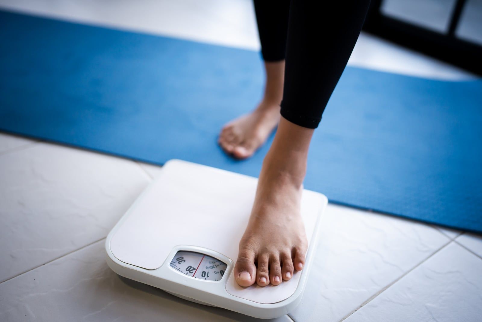 Person standing barefoot on a digital scale on a blue exercise mat.