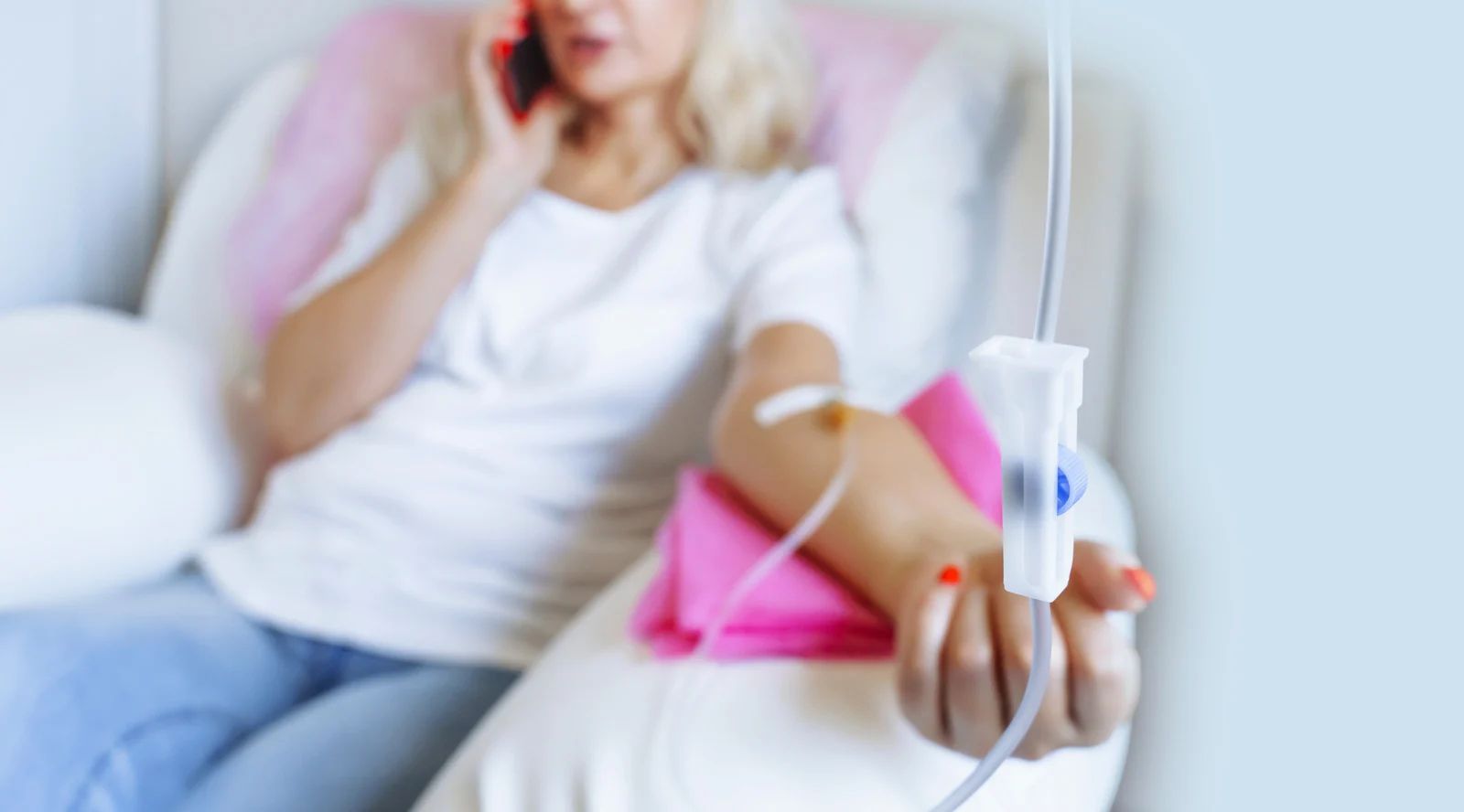 Woman lying in a hospital bed receiving an IV infusion, with a pink blanket nearby.