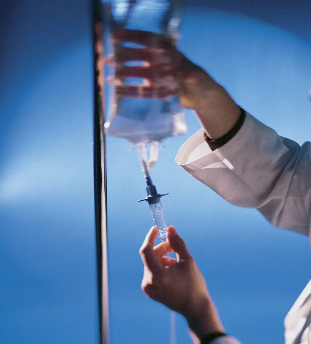 Healthcare worker filling a syringe from an IV bag against a blue background