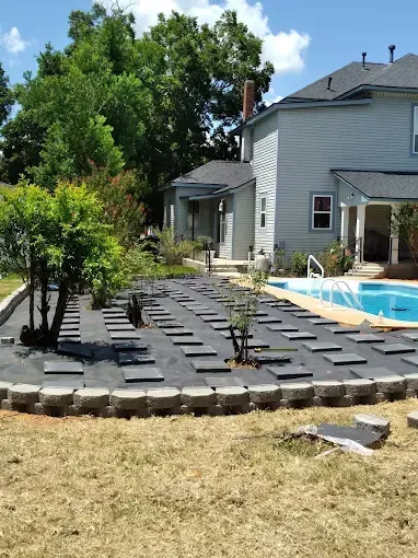 Backyard patio with dark stepping stones, small trees, and a pool beside a gray house