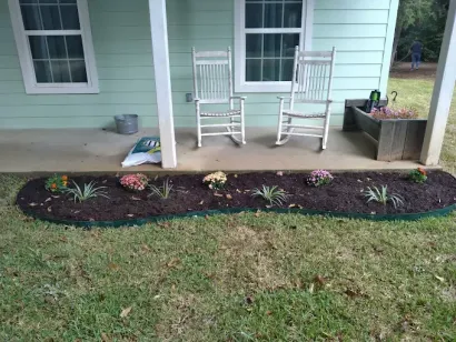 Front porch with two white rocking chairs, potted planter, and a flower bed along the lawn