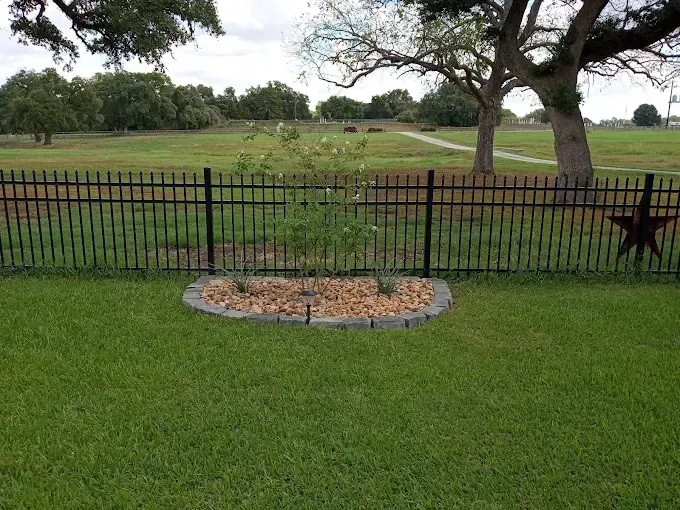 Black metal fence with star decoration in a grassy yard, trees and open field beyond.