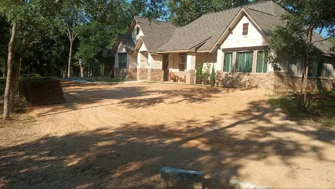 Single-story house with a large dirt yard, trees, and a shaded porch in the background.