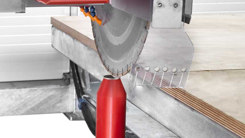 Close-up of CNC bridge saw blade cutting stone slab with water nozzles for cooling and a red support post for stability.