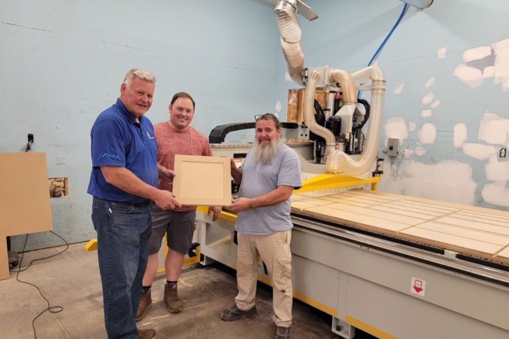 three men are standing in front of a machine holding a piece of wood .