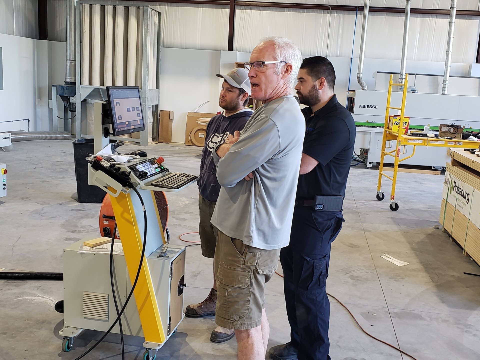 Three individuals standing next to industrial equipment with a monitor.
