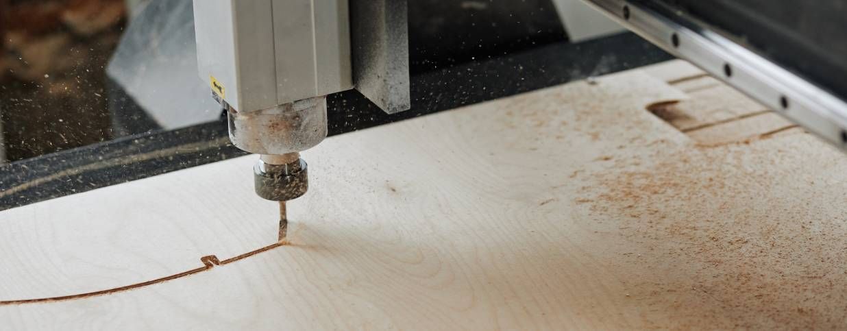CNC wood router boring into wood, with sawdust particles scattered in the air.