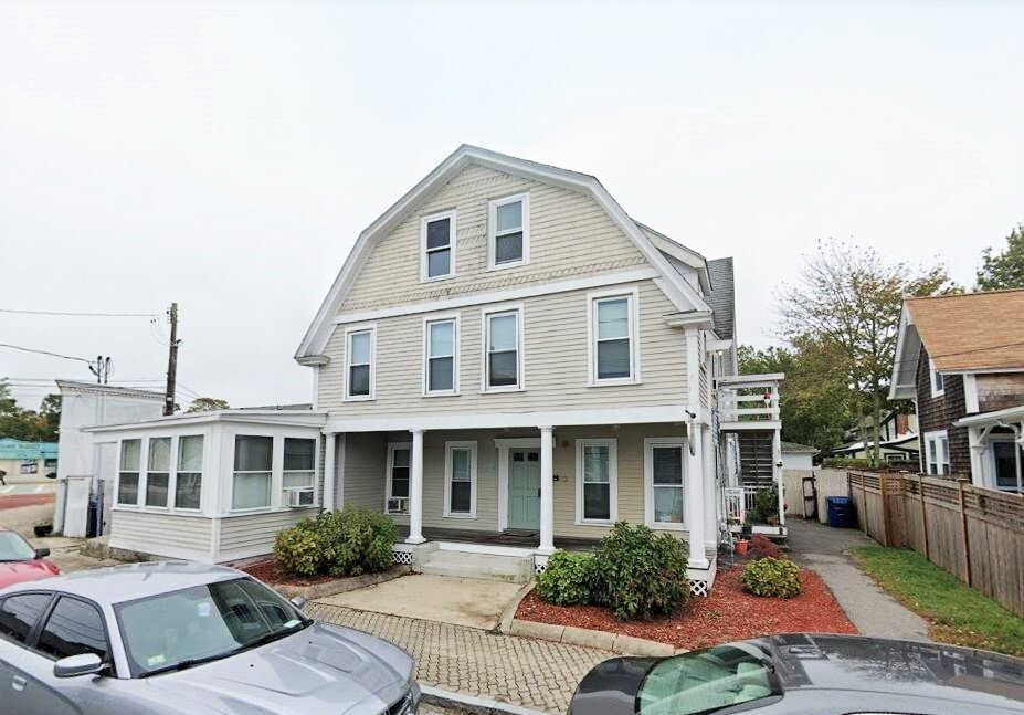 A car is parked in front of a large house.