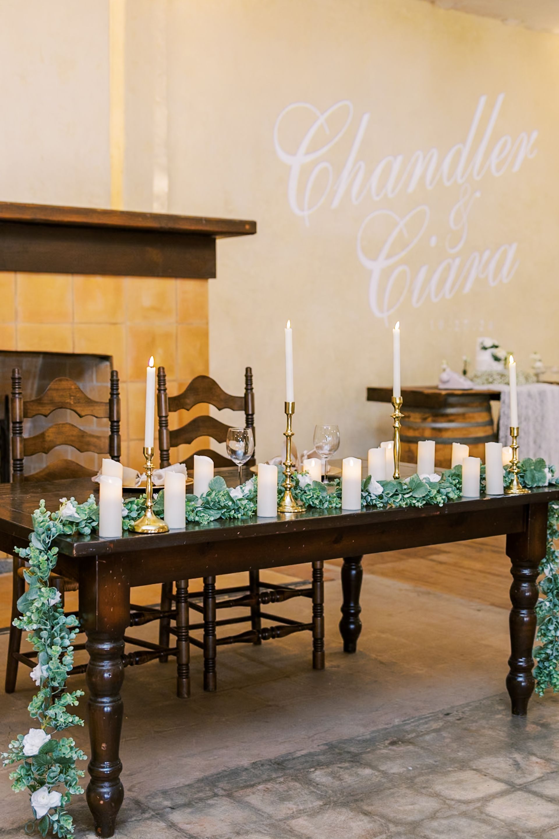 Decorated wooden table with white candles and greenery in a beige room with “Chandler & Clara” on the wall