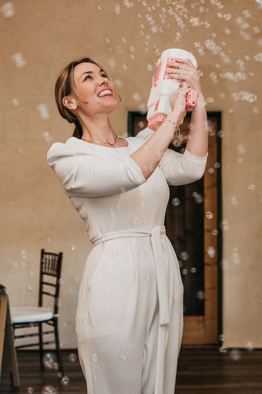 Woman in a white dress smiling and spraying confetti indoors during a celebration