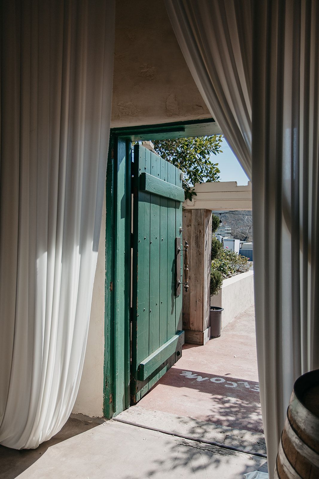 Curtained doorway opening to a sunlit patio with a green gate and stone path