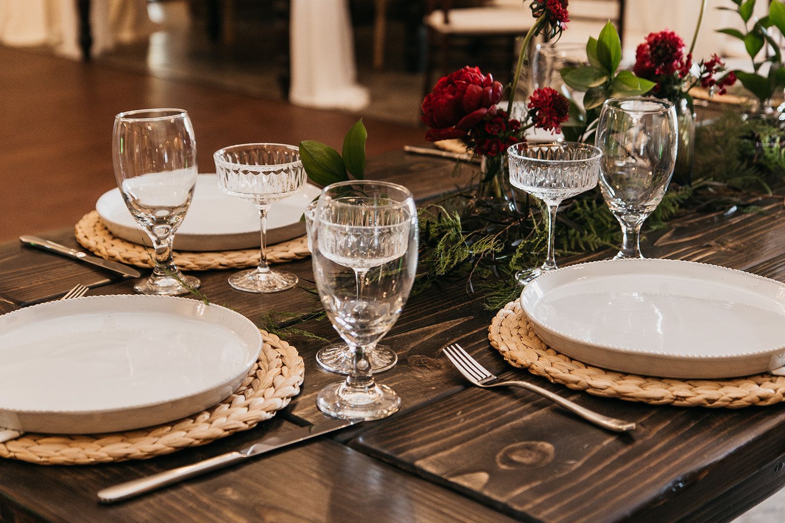 Elegant dining table set with white plates, glassware, and red floral centerpiece