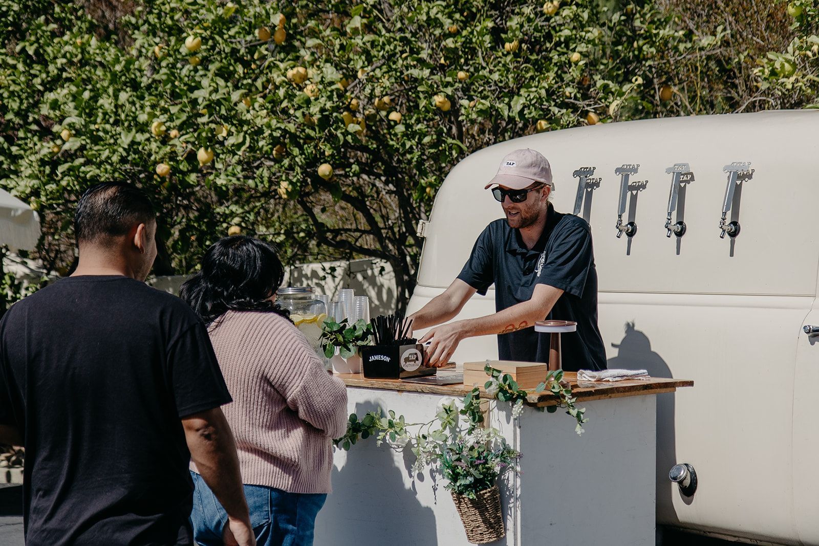 Barista serving coffee at an outdoor cart to customers in a garden setting