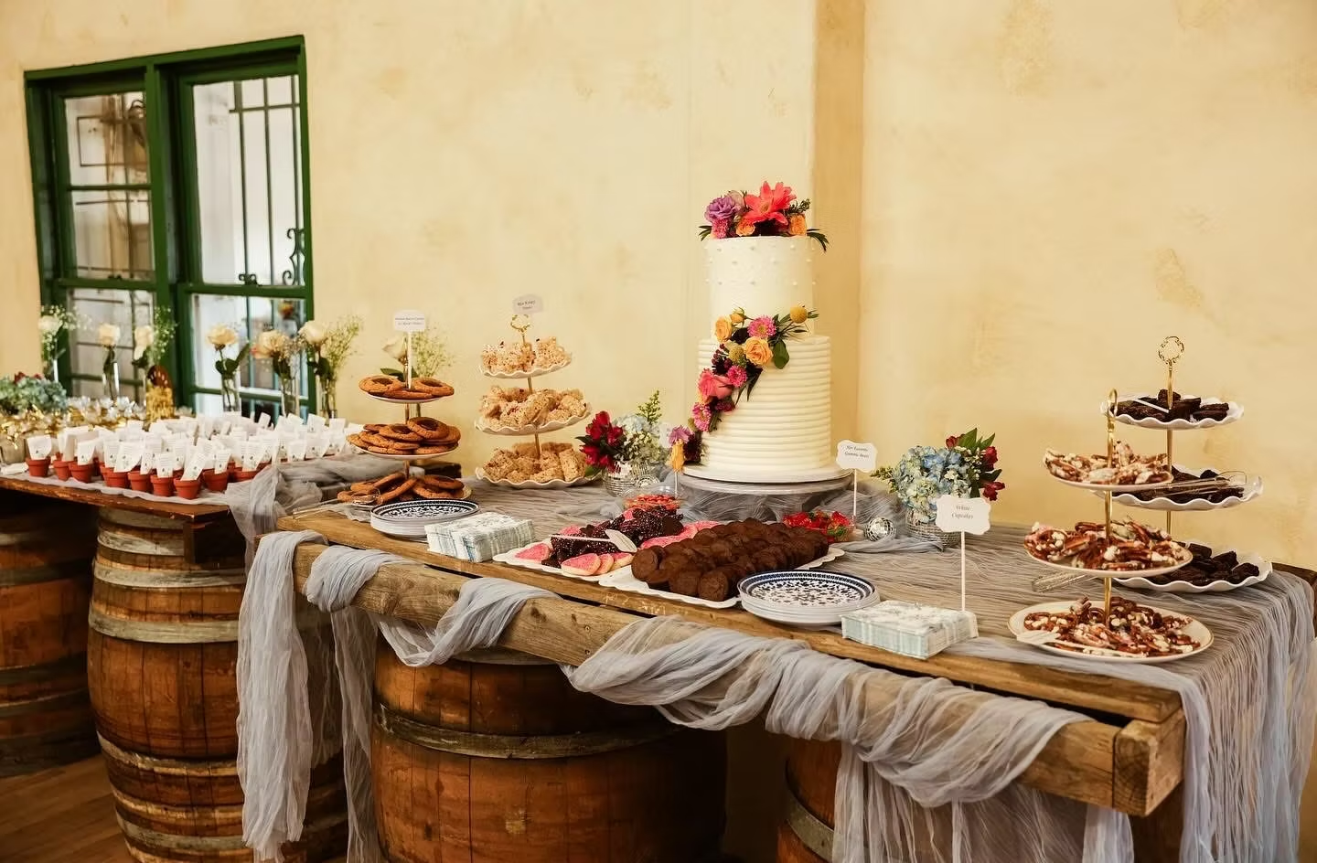 Dessert buffet on rustic tables with cakes, pastries, and floral decor in a warm indoor room