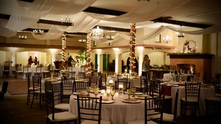 Decorated banquet hall with round tables, chairs, and warm string lighting overhead