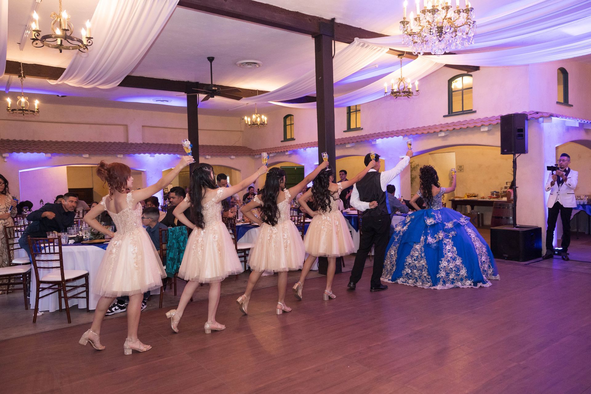Children performing a dance routine in a decorated banquet hall with chandeliers and guests watching