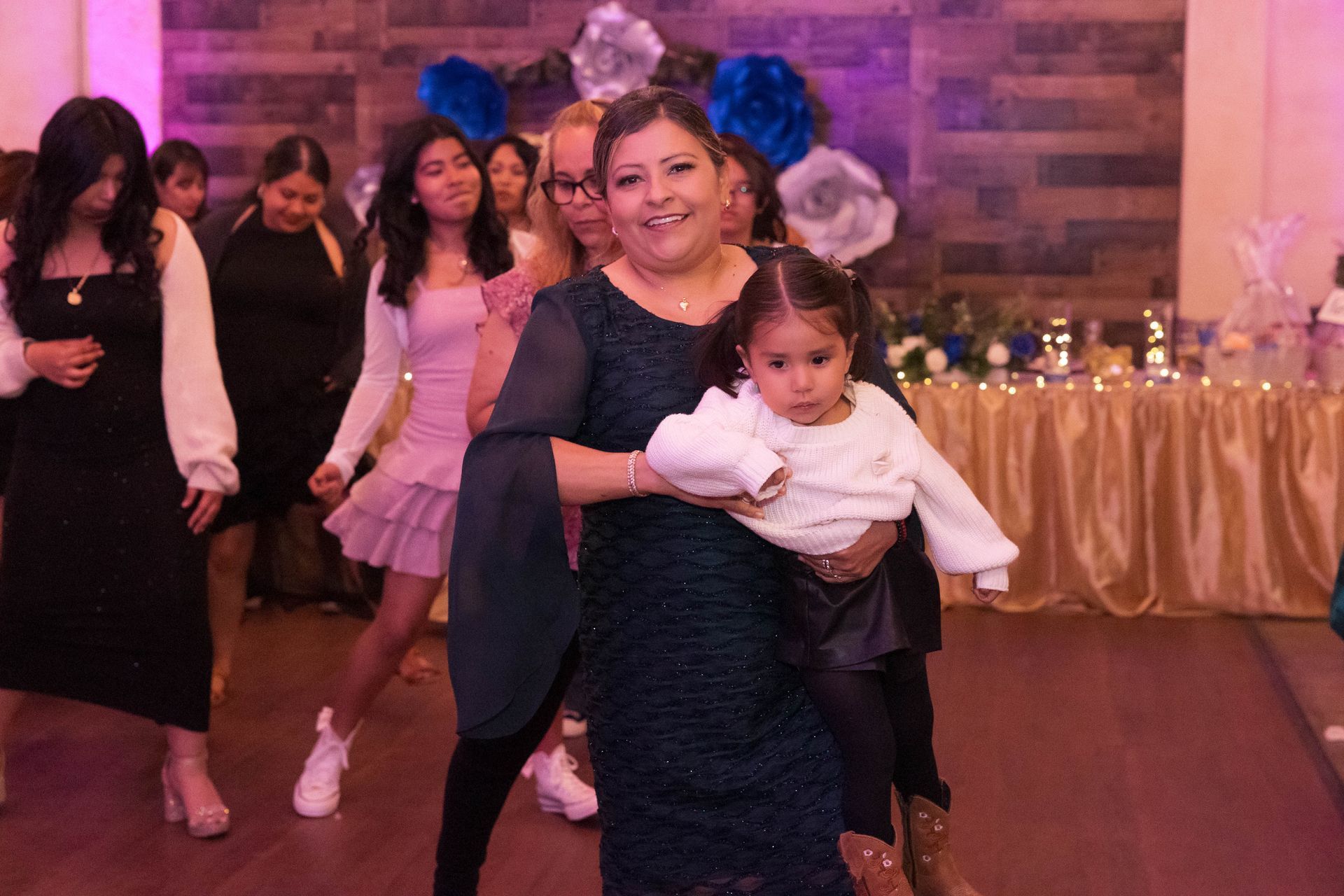 Woman holding a baby dancing in a decorated event hall with people in the background