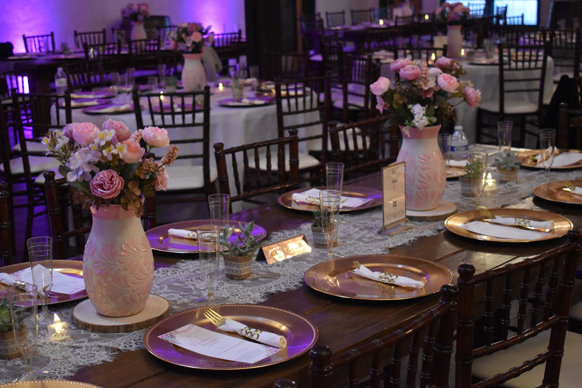 Elegant banquet tables set with white plates, candles, and pink floral centerpieces in a softly lit reception hall