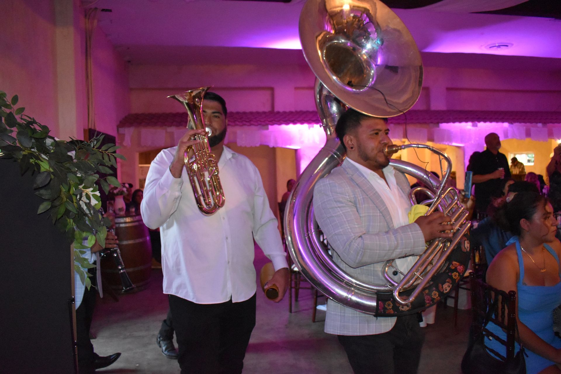 Brass band performing indoors under pink lighting, with a trombone and a sousaphone in the foreground