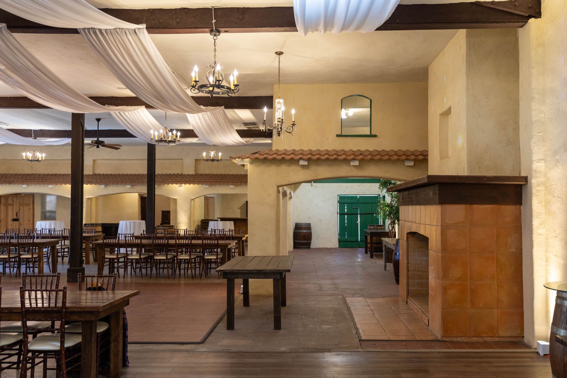 Empty rustic dining hall with wooden tables, draped ceiling fabric, and a large fireplace mantel