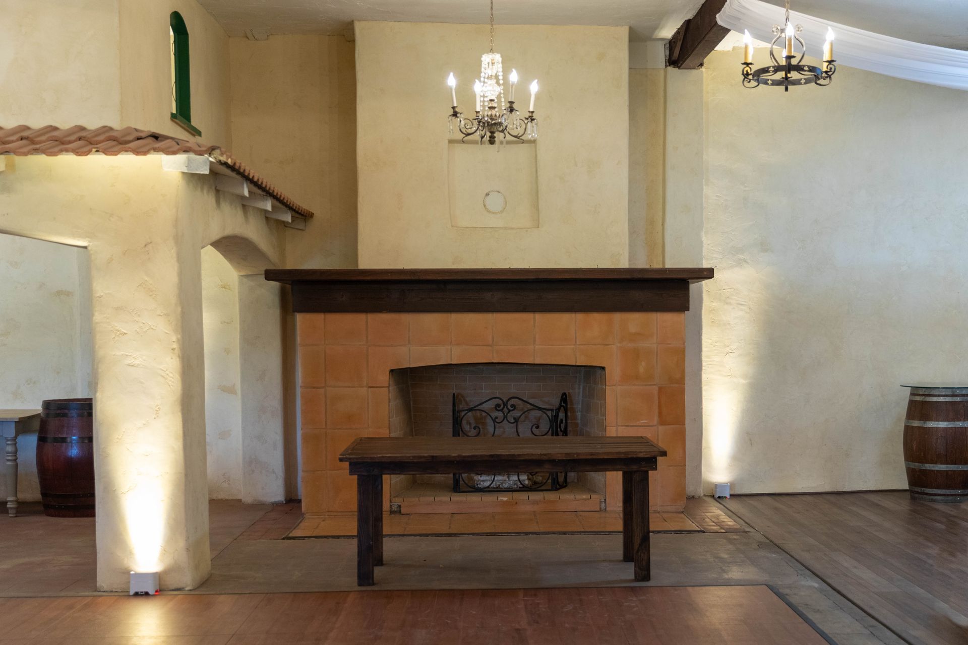 Rustic room with a fireplace, bench, wooden beams, and chandelier illuminated by wall sconces